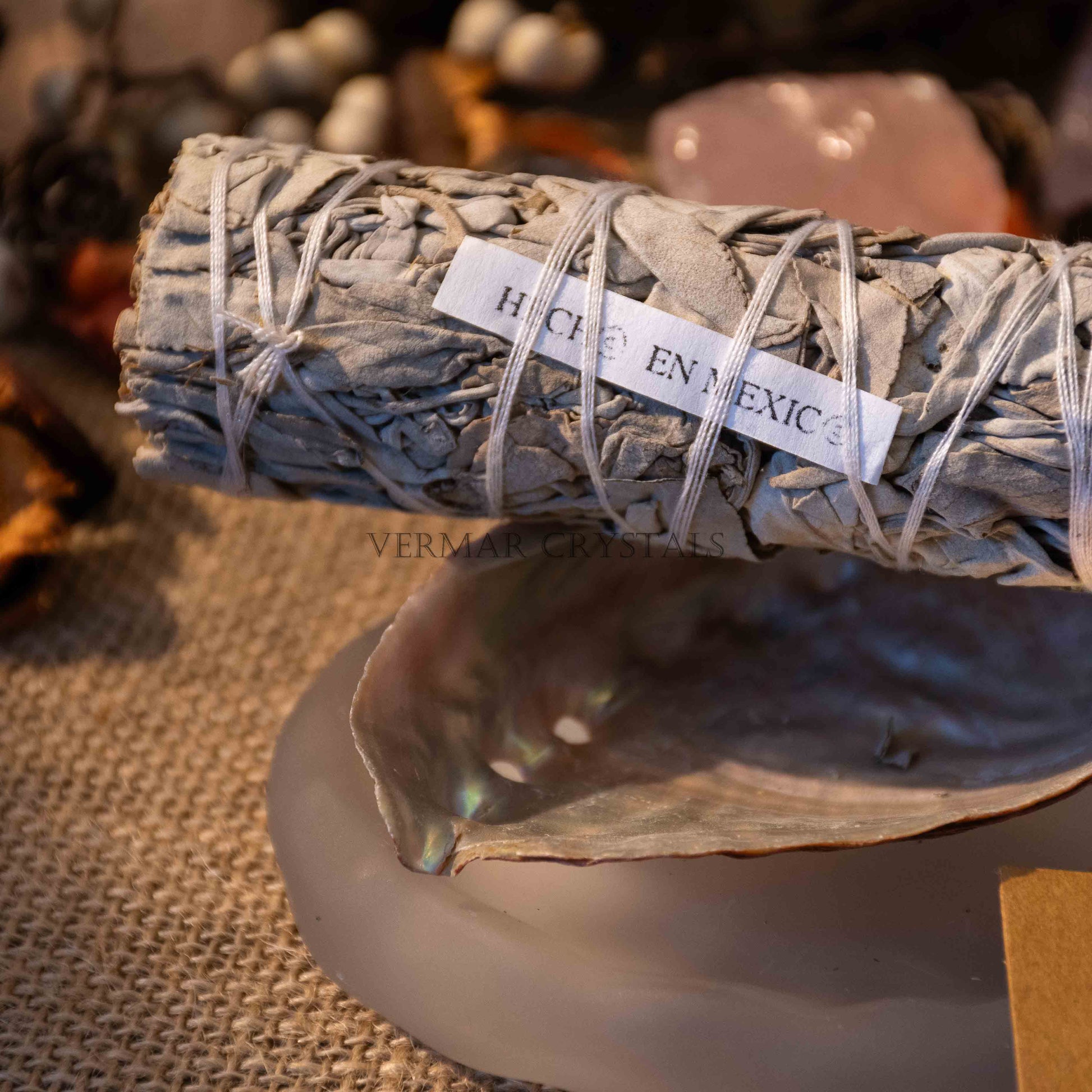 Close-up of premium white sage smudge stick resting on an abalone shell with crystals and natural decor background