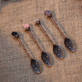 Four antique bronze spoons with floral engravings and crystal accents on woven burlap background