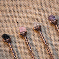 Handcrafted antique bronze alchemy spoons each topped with a different raw crystal on textured burlap background