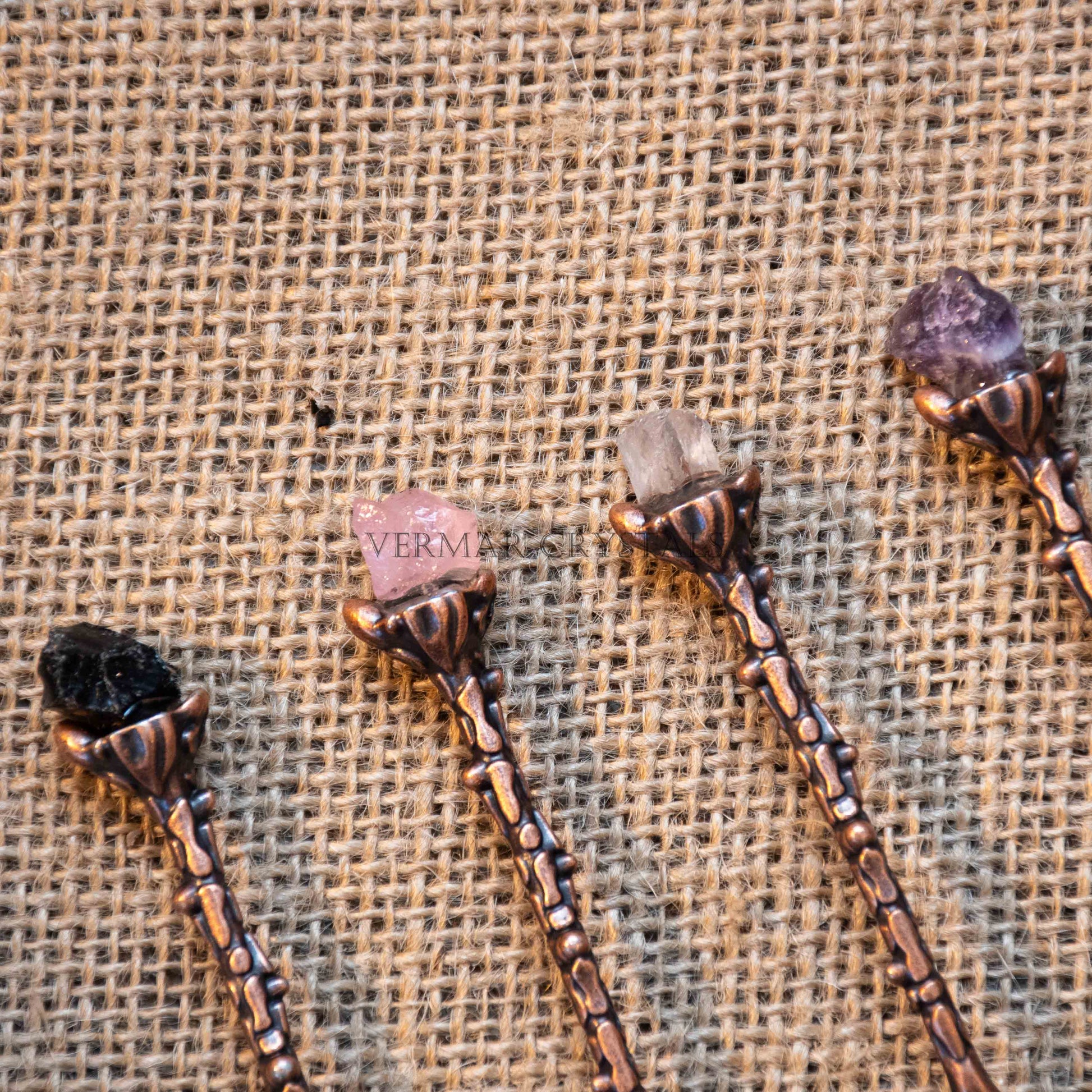 Handcrafted antique bronze alchemy spoons each topped with a different raw crystal on textured burlap background