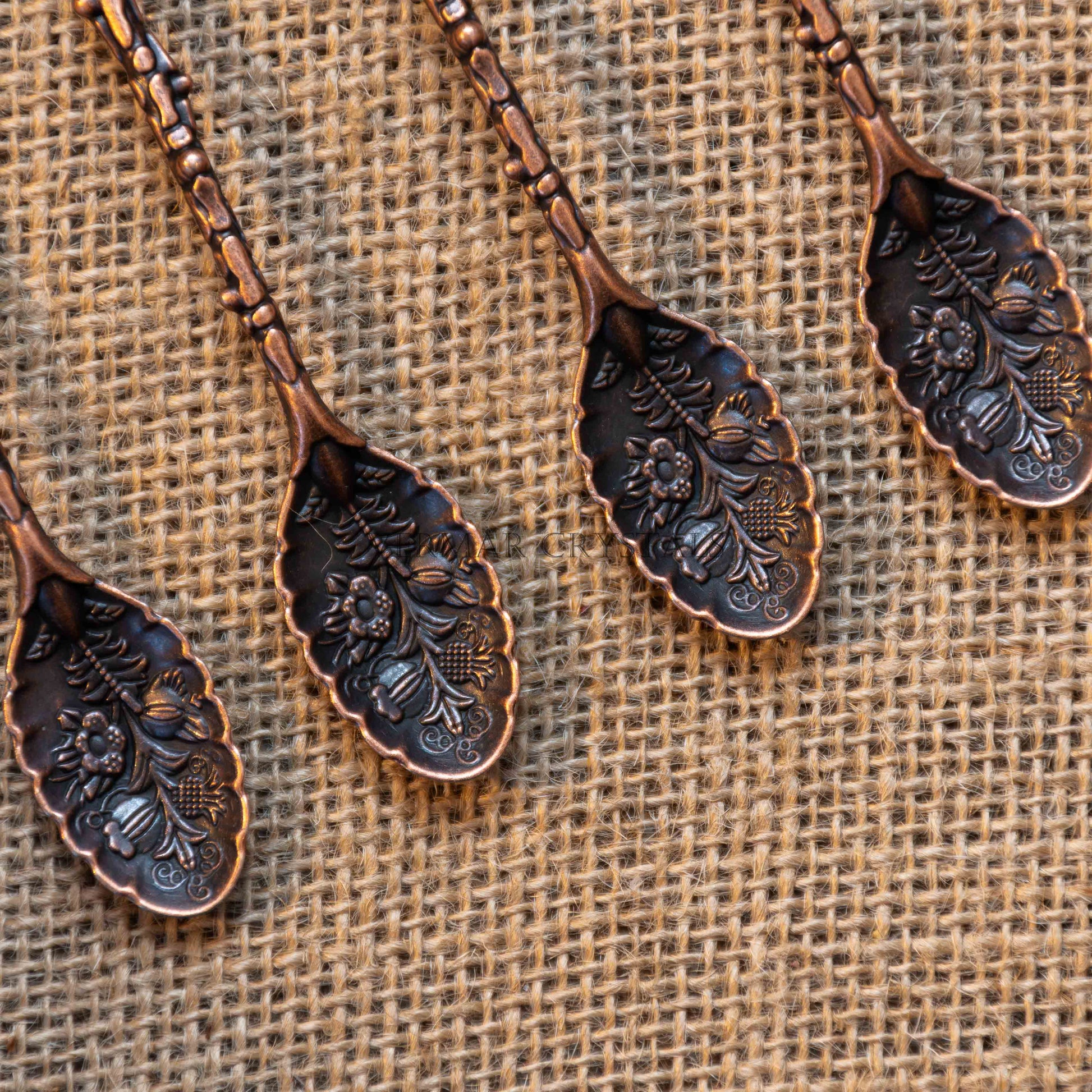 Close-up of antique bronze-tone alchemy spoons with floral engravings arranged on burlap fabric background