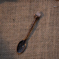 Antique bronze alchemy spoon with floral engravings and raw rose quartz crystal on rustic burlap background