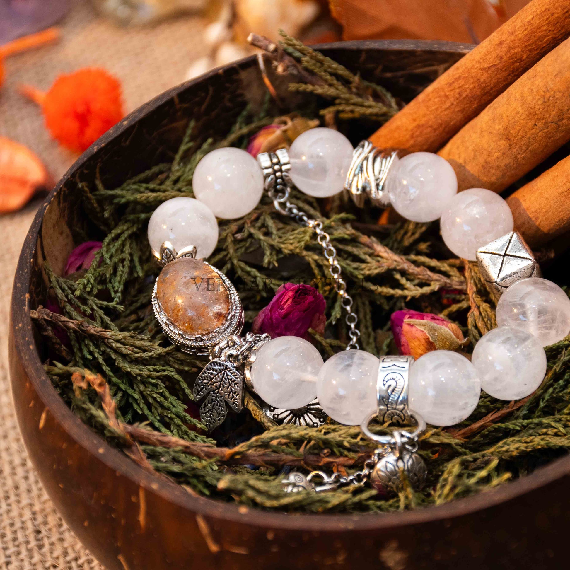 White and Garden Phantom Quartz bracelet with silver charms resting on dried greenery inside wooden bowl with cinnamon sticks