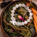 Round Phantom Quartz and Clear Quartz bead bracelet with silver butterfly charm on natural greenery and dried rose petals background