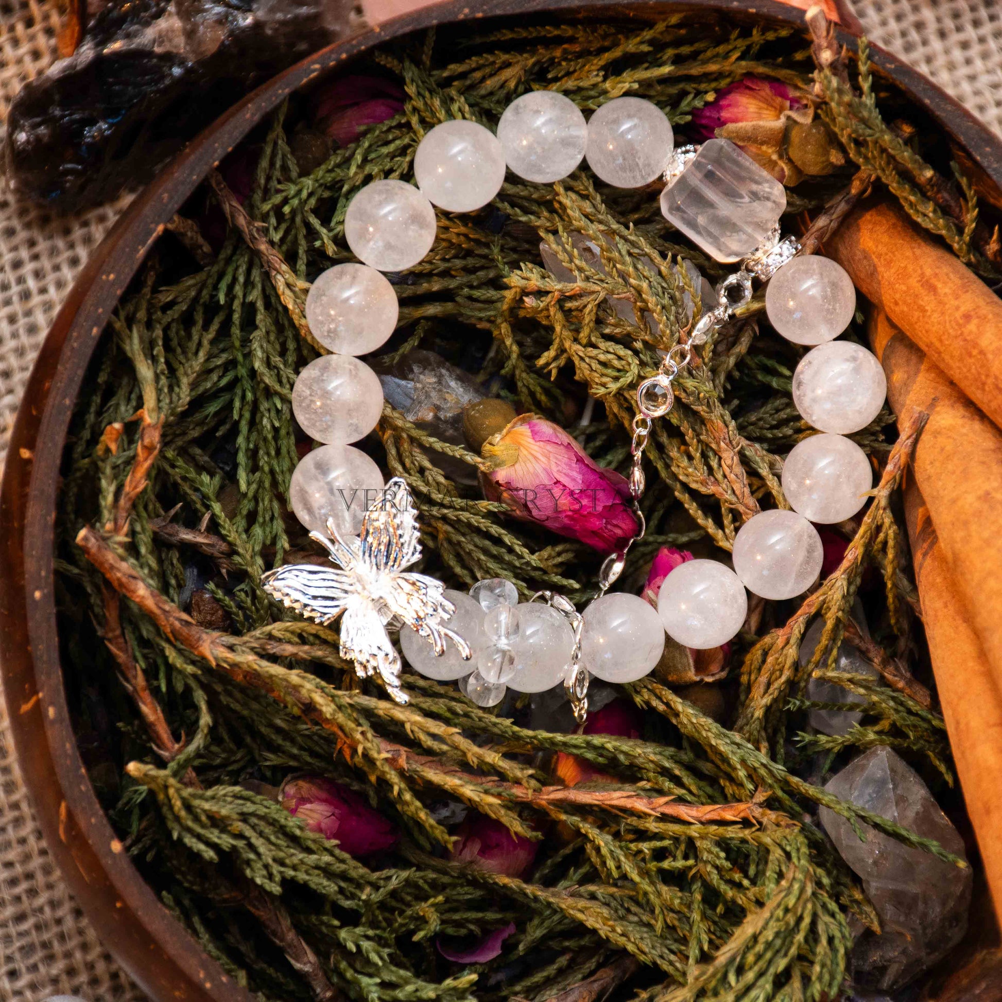 Round Phantom Quartz and Clear Quartz bead bracelet with silver butterfly charm on natural greenery and dried rose petals background