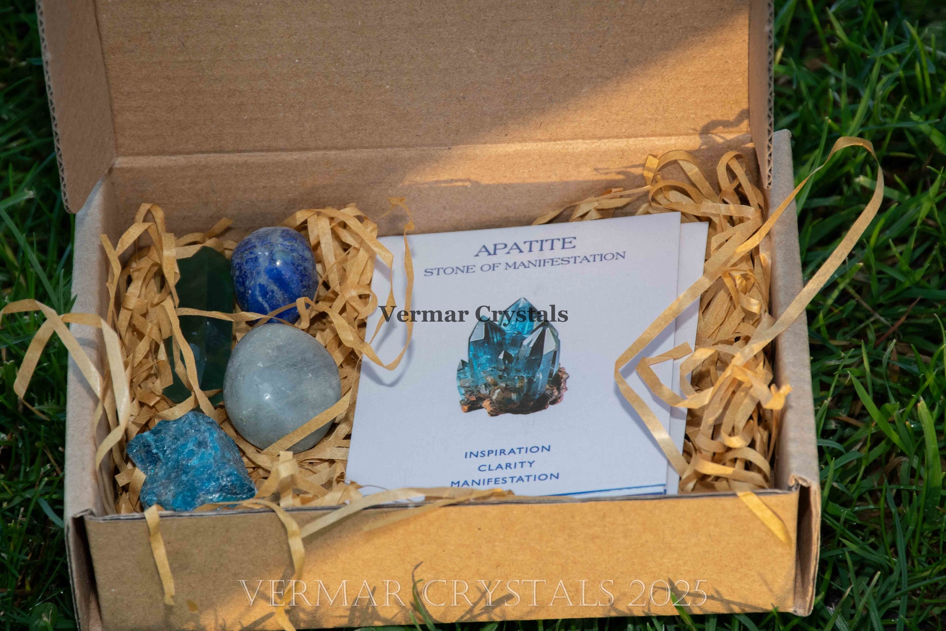 Set of polished blue and turquoise Apatite stones in craft box with information card on grass background