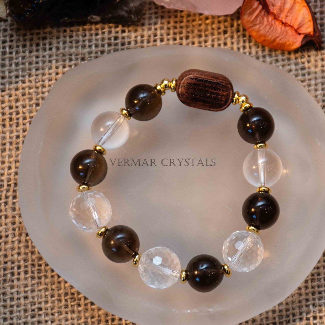 Close-up of Earthbound Light Bracelet with smoky quartz, clear quartz, and natural wood beads on burlap with crystals background