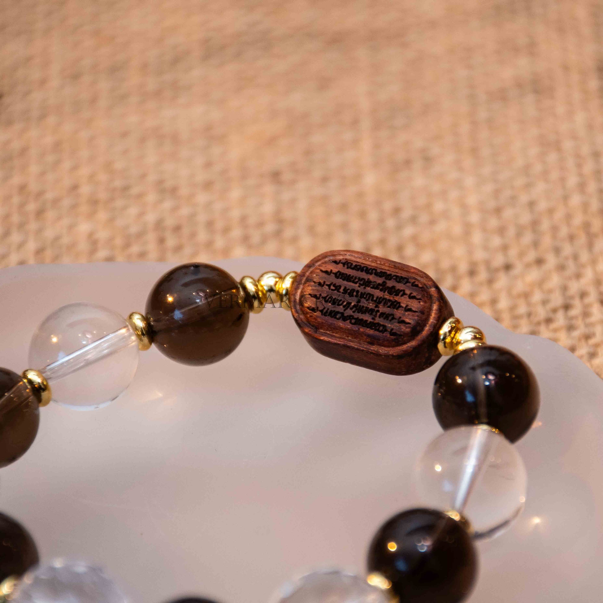 Close-up of Earthbound Light Bracelet featuring 12mm smoky quartz, clear quartz, natural wood bead, and gold spacer beads on white dish