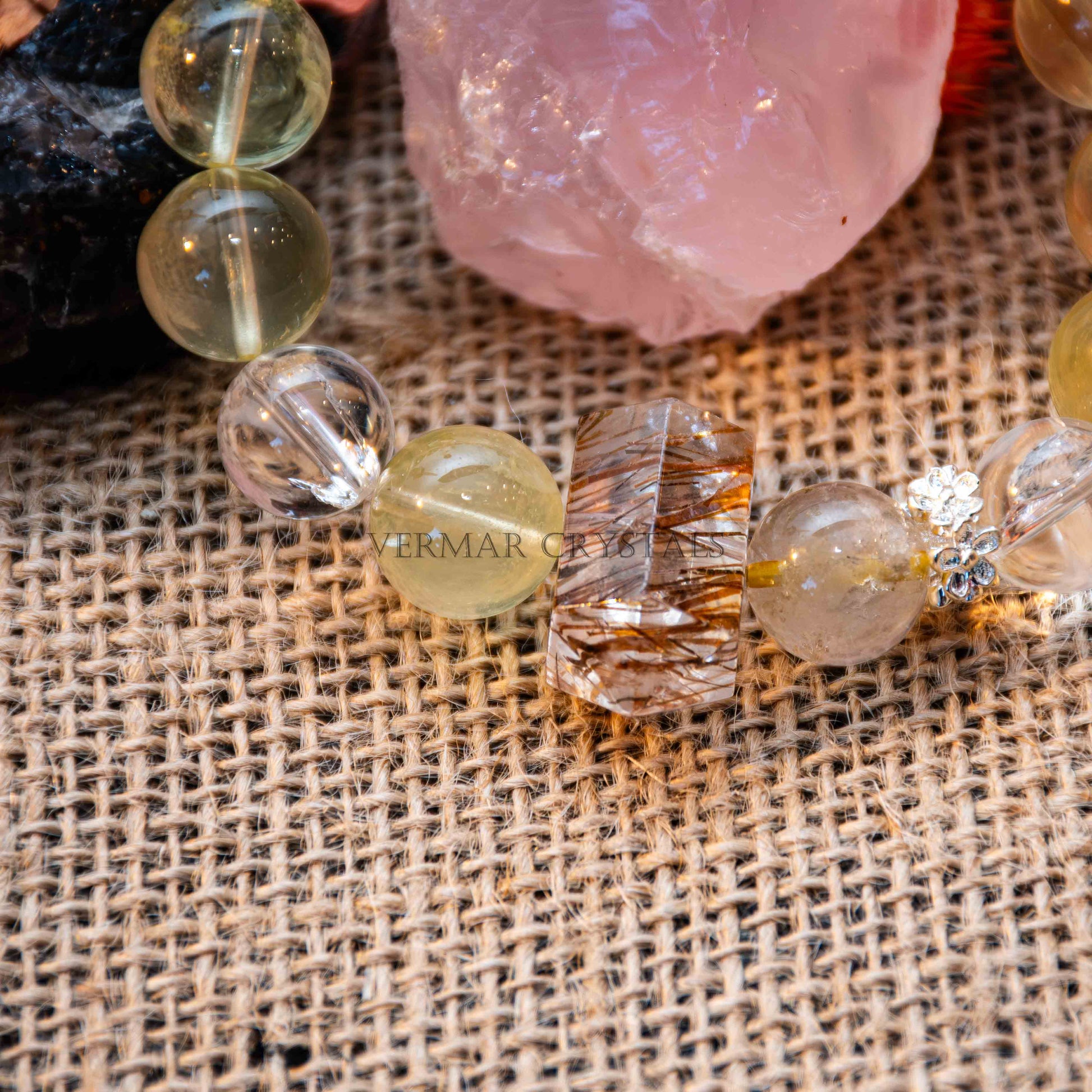 Close-up of handcrafted Citrine and Phantom Quartz beads on a woven fabric surface with a pink crystal in background