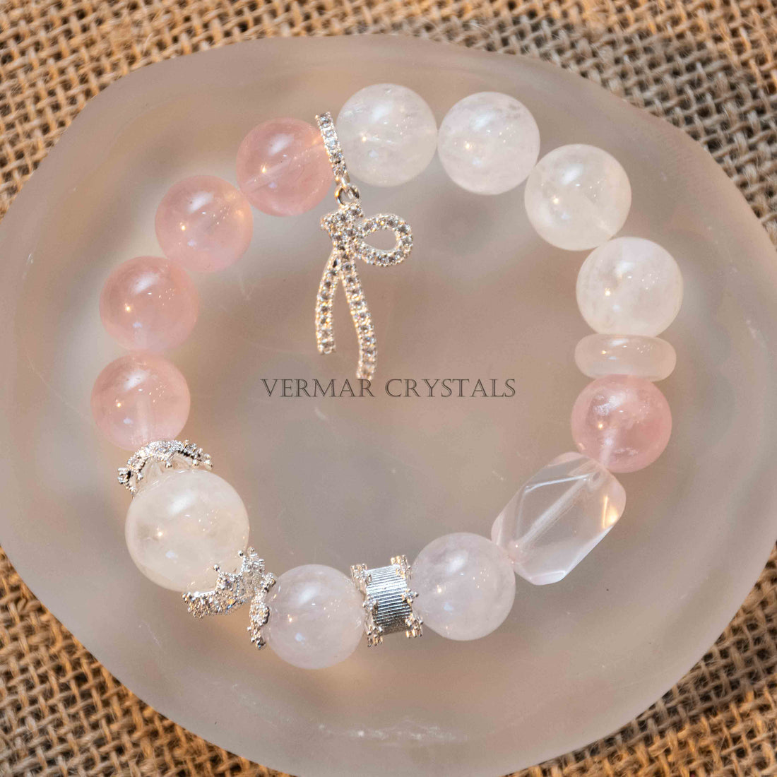 Round rose quartz and white phantom quartz beads bracelet with silver charm on natural woven surface