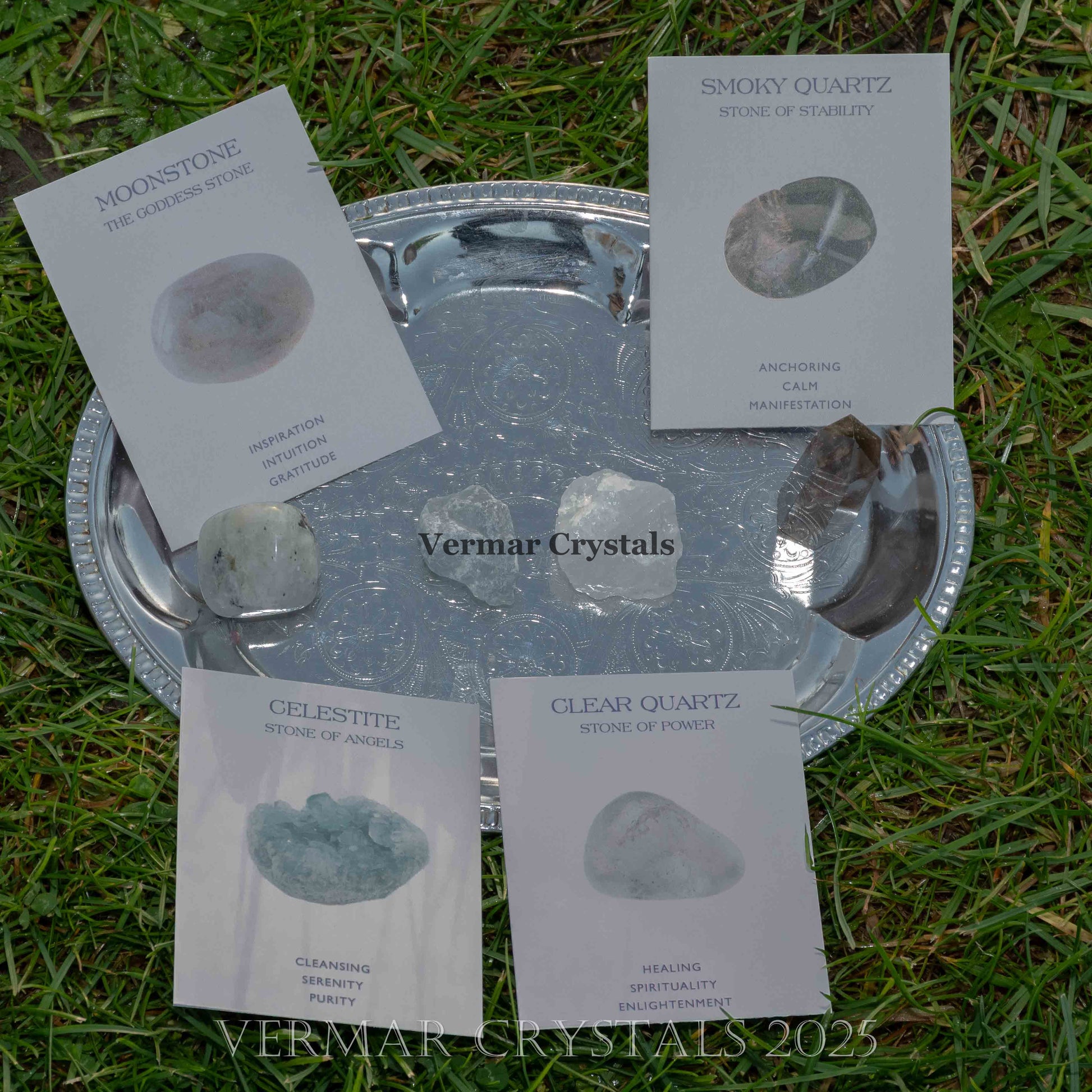 Collection of polished moonstone, smoky quartz, celestite, and clear quartz crystals on a silver tray outdoors on grass background