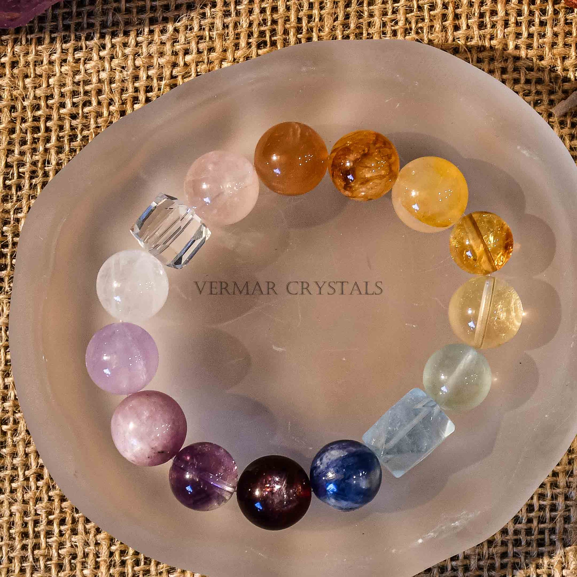 Rainbow gradient multi-gemstone bracelet with large polished beads displayed on a frosted crystal dish over burlap background