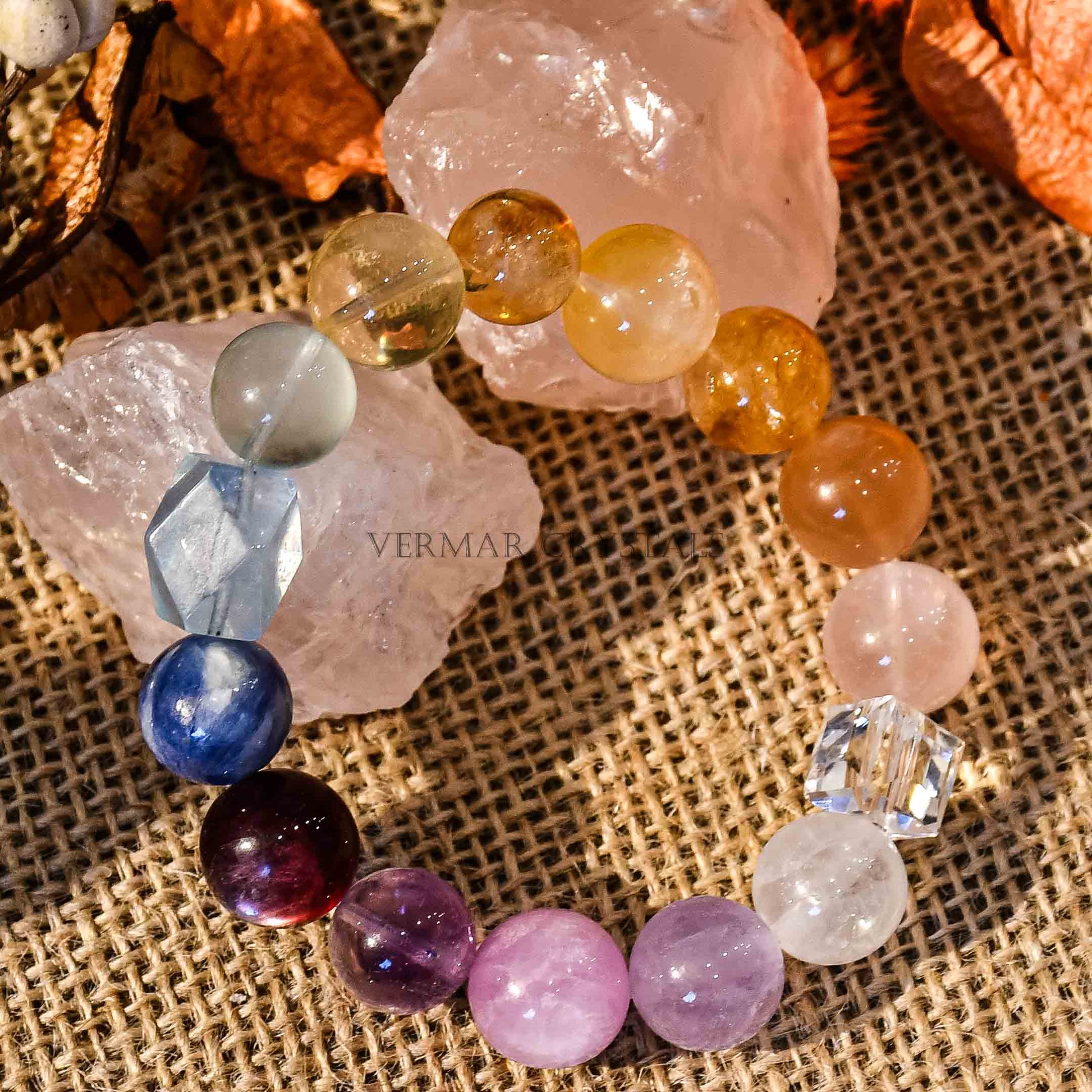 Rainbow gradient gemstone bracelet with large polished beads displayed on burlap with rose quartz crystals