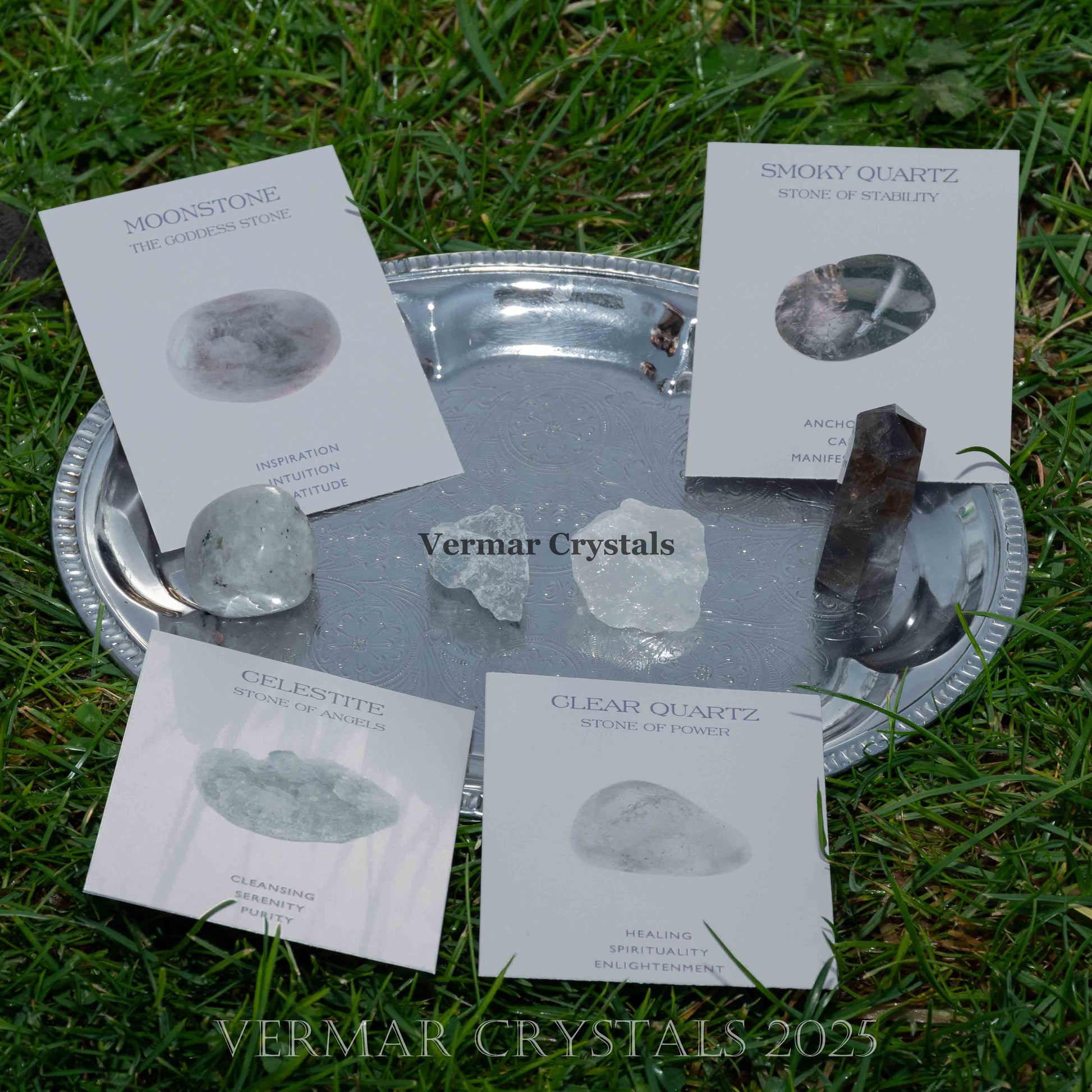 Set of natural rough moonstone, smoky quartz, celestite, and clear quartz crystals on a silver tray outdoors