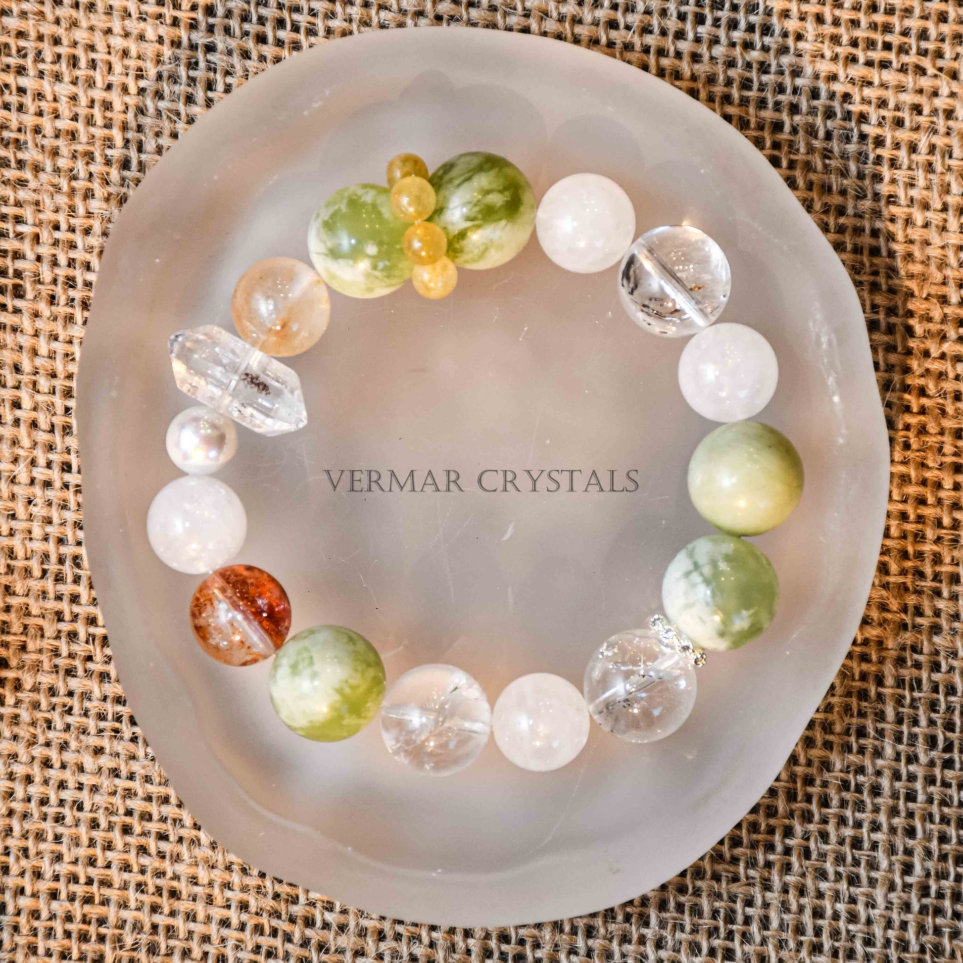 Round beaded bracelet with fresh green and cream white serpentine jade, clear quartz, and yellow accent beads on frosted dish