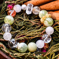 Close-up of fresh green and cream white serpentine jade bracelet with clear and amber beads on pine branches background