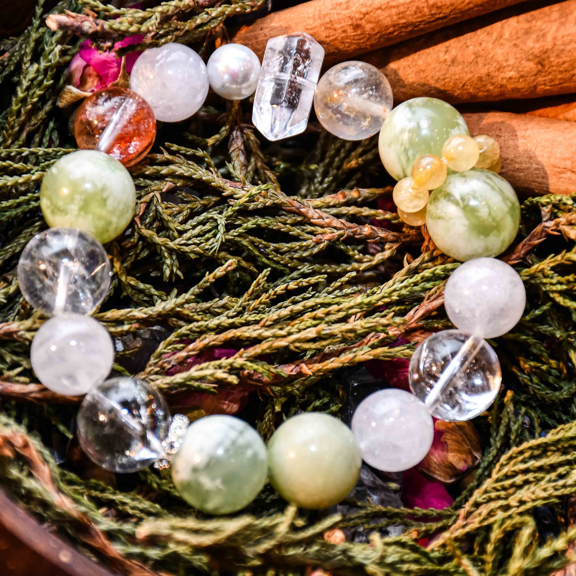 Close-up of fresh green and cream white serpentine jade bracelet with clear and amber beads on pine branches background