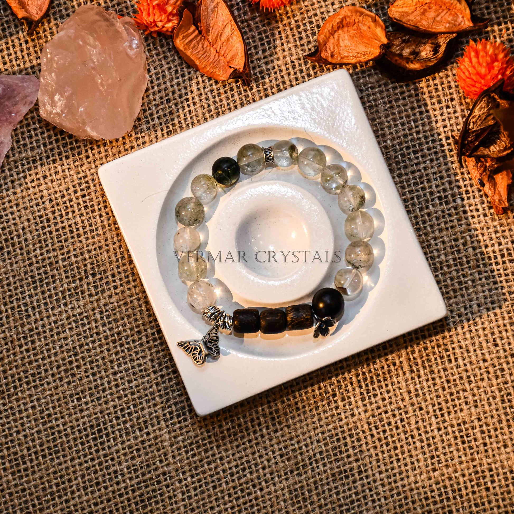Beaded bracelet with clear and black stones, silver butterfly charm, and black skull bead on white ceramic dish with natural decor
