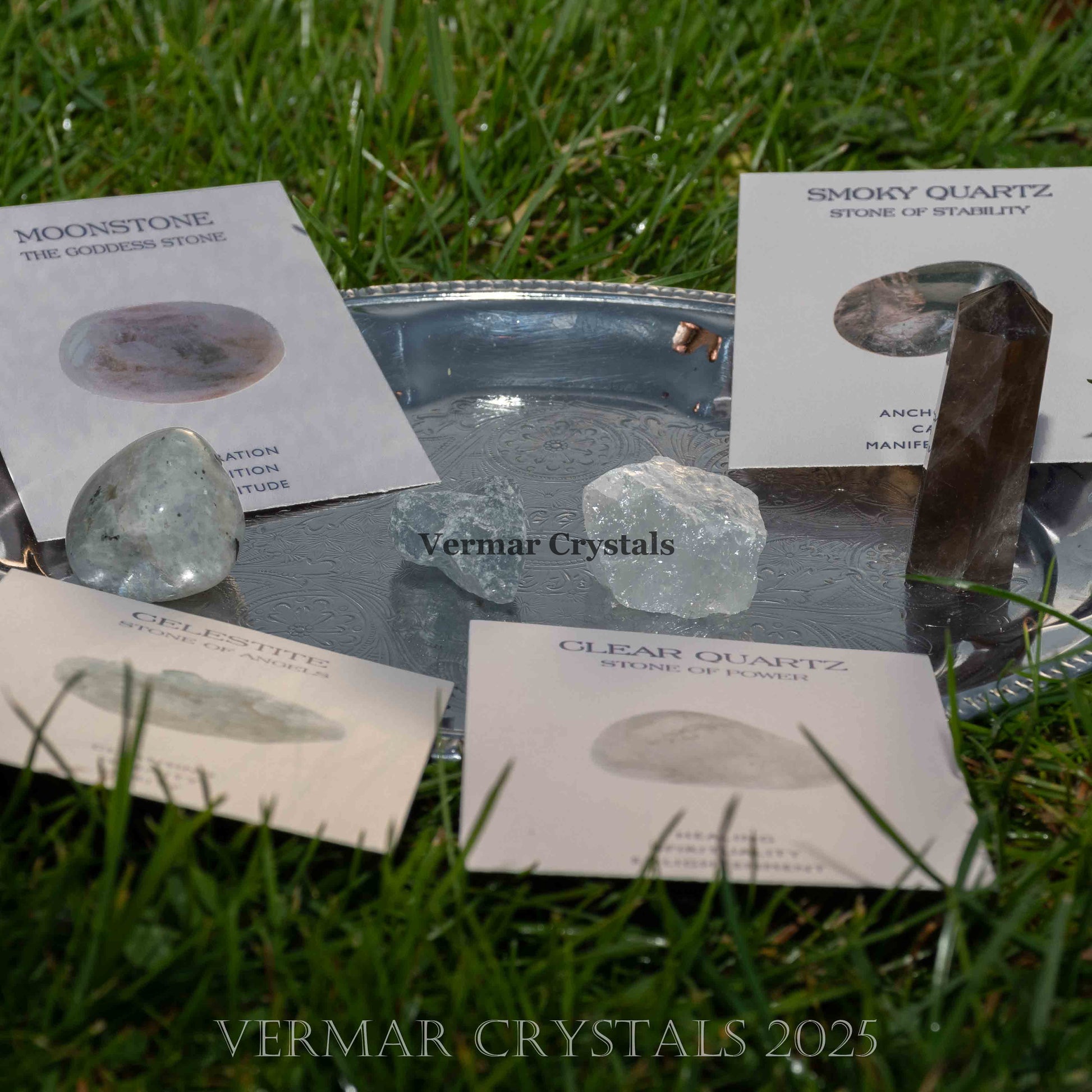 Set of natural health and wellness crystals including moonstone, smoky quartz, and clear quartz on metal tray outdoors