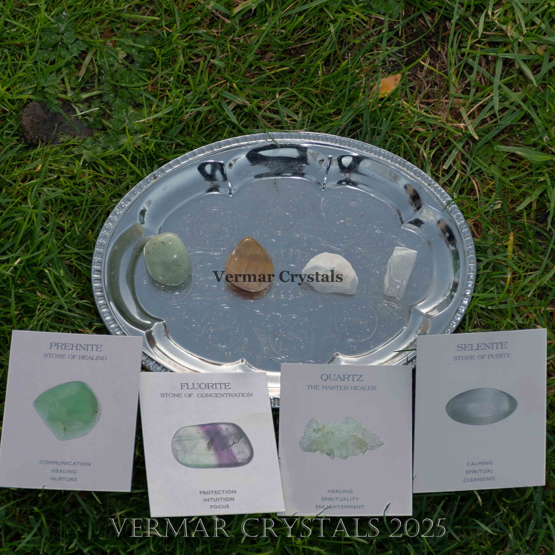 Set of four healing crystals including prehnite, fluorite, quartz, and selenite displayed on a silver tray outdoors