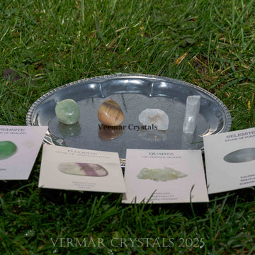 Set of four polished healing crystals including green fluorite, golden tiger's eye, clear quartz, and selenite on silver tray outdoors