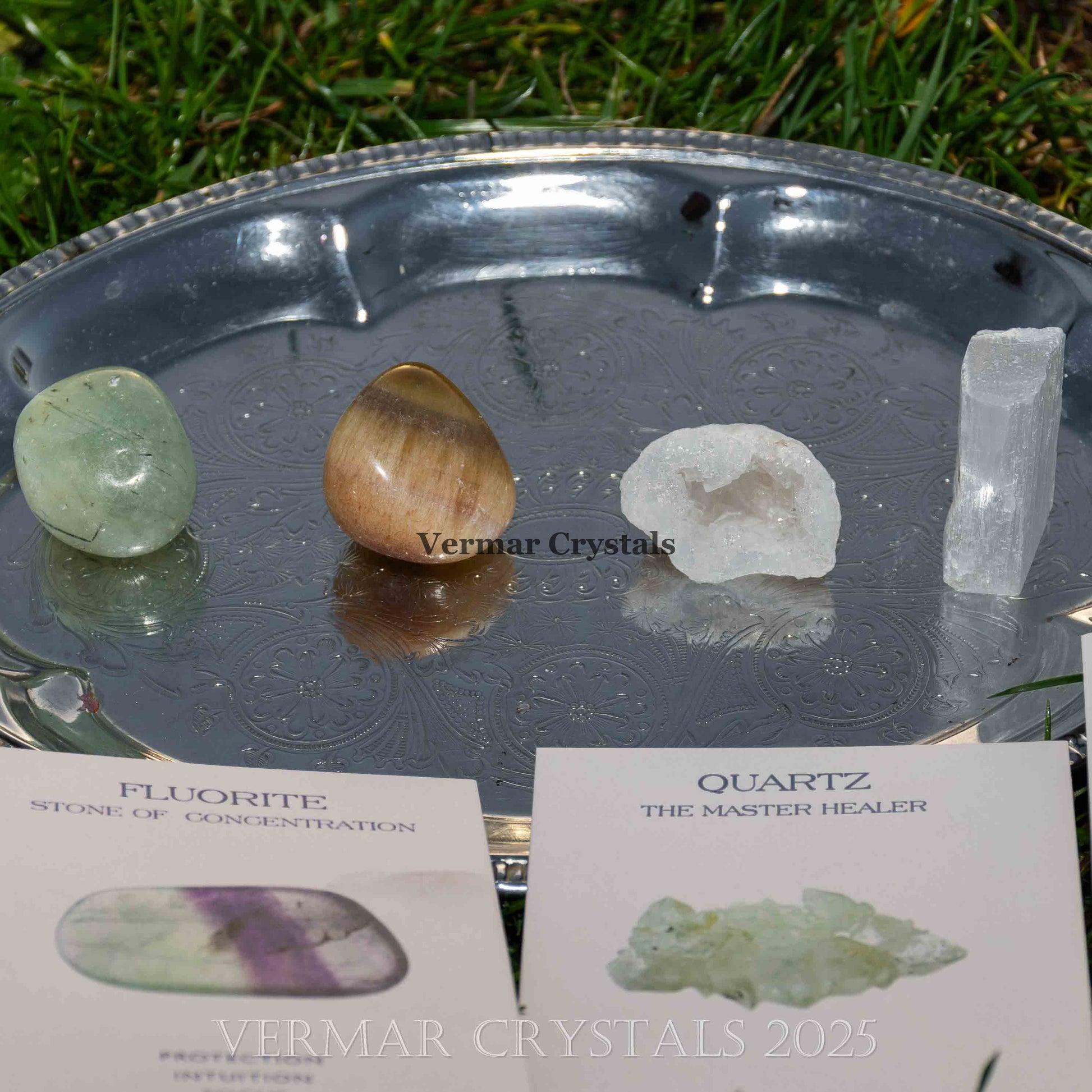 Set of polished and raw green fluorite, brown tiger's eye, white quartz, and selenite crystals on a silver tray outdoors