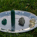 Set of natural crystals including green polished tower, rough stones on decorative silver tray outdoors on grass background