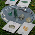 Set of natural crystals including green aventurine, pyrite, malachite, citrine, and prosperity stones on silver tray outdoors