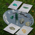 Silver tray displaying a collection of polished green and golden prosperity crystals with descriptive cards on grass background