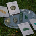 Set of natural crystals including citrine, pyrite, green aventurine, and malachite displayed on silver tray outdoors