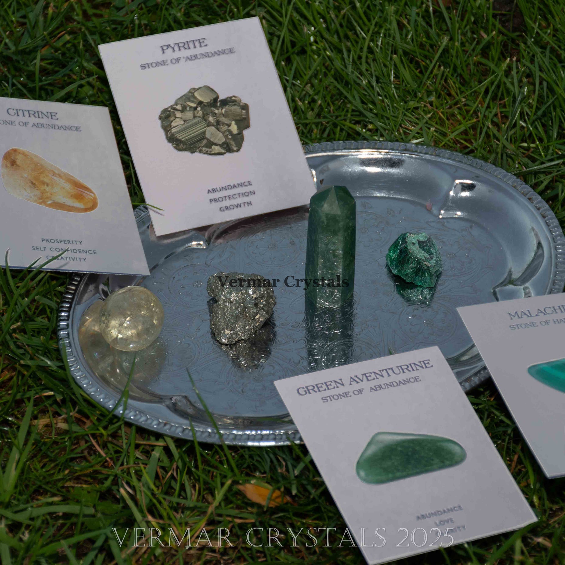 Set of natural crystals including citrine, pyrite, green aventurine, and malachite displayed on silver tray outdoors