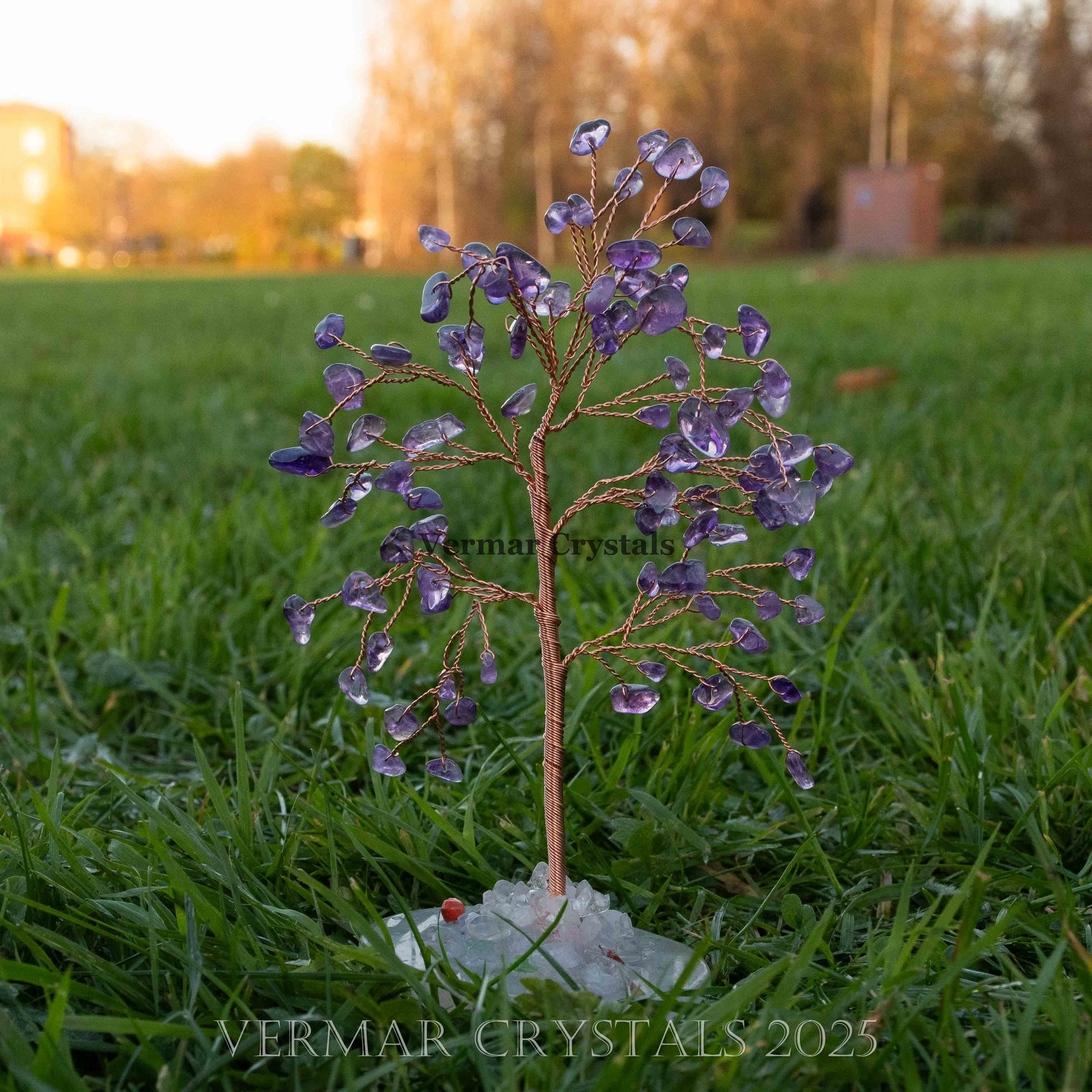 Handmade decorative tree with natural amethyst crystal leaves and rough white agate stone base on grass background