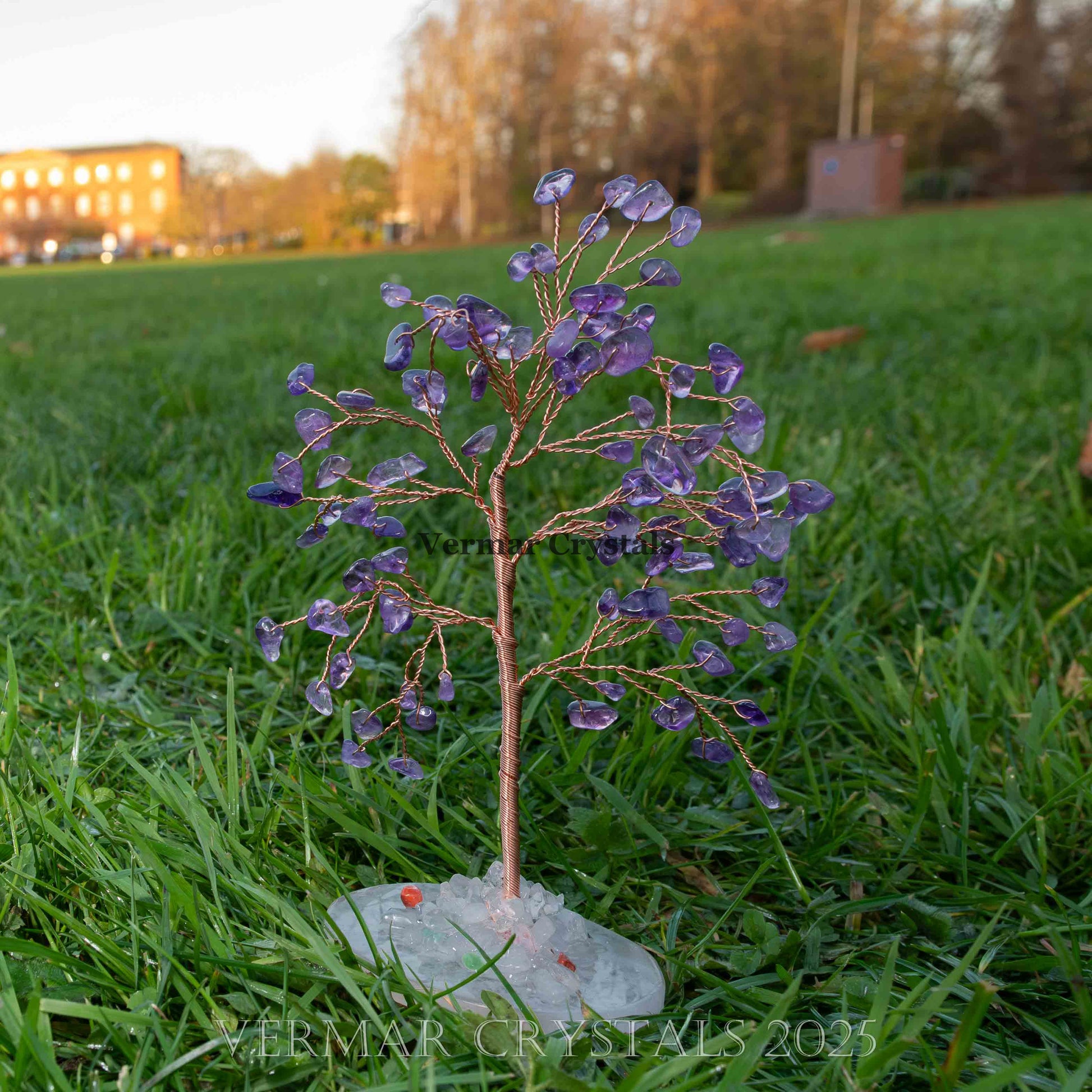 Handmade amethyst crystal tree with polished purple gemstone leaves and white agate base on grass outdoors