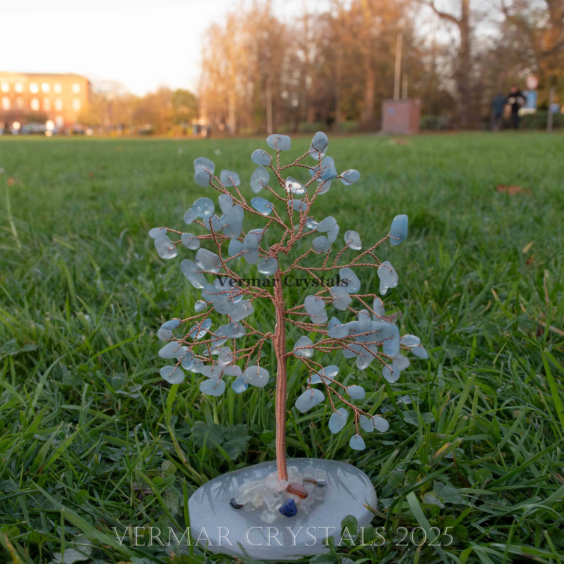 Handmade small aquamarine crystal tree with twisted copper wire branches on polished natural agate base outdoors