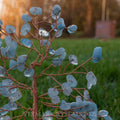 Handmade aquamarine crystal tree with polished blue gemstones and twisted copper wire branches on natural agate base outdoors