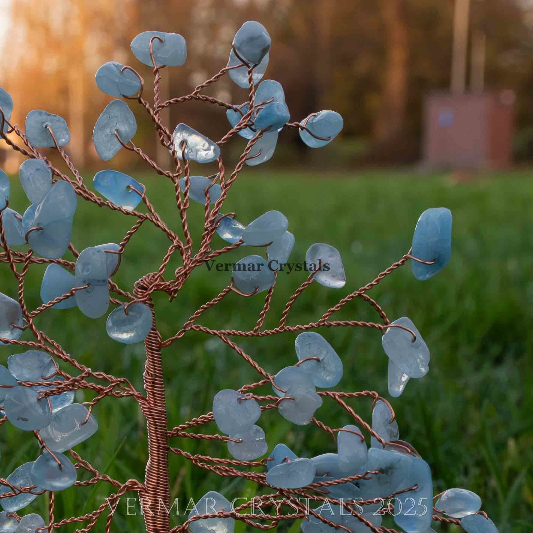 Handmade aquamarine crystal tree with polished blue gemstones and twisted copper wire branches on natural agate base outdoors