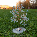 Handmade aquamarine crystal tree with natural blue gemstones and copper wire branches on round agate base outdoors on grass