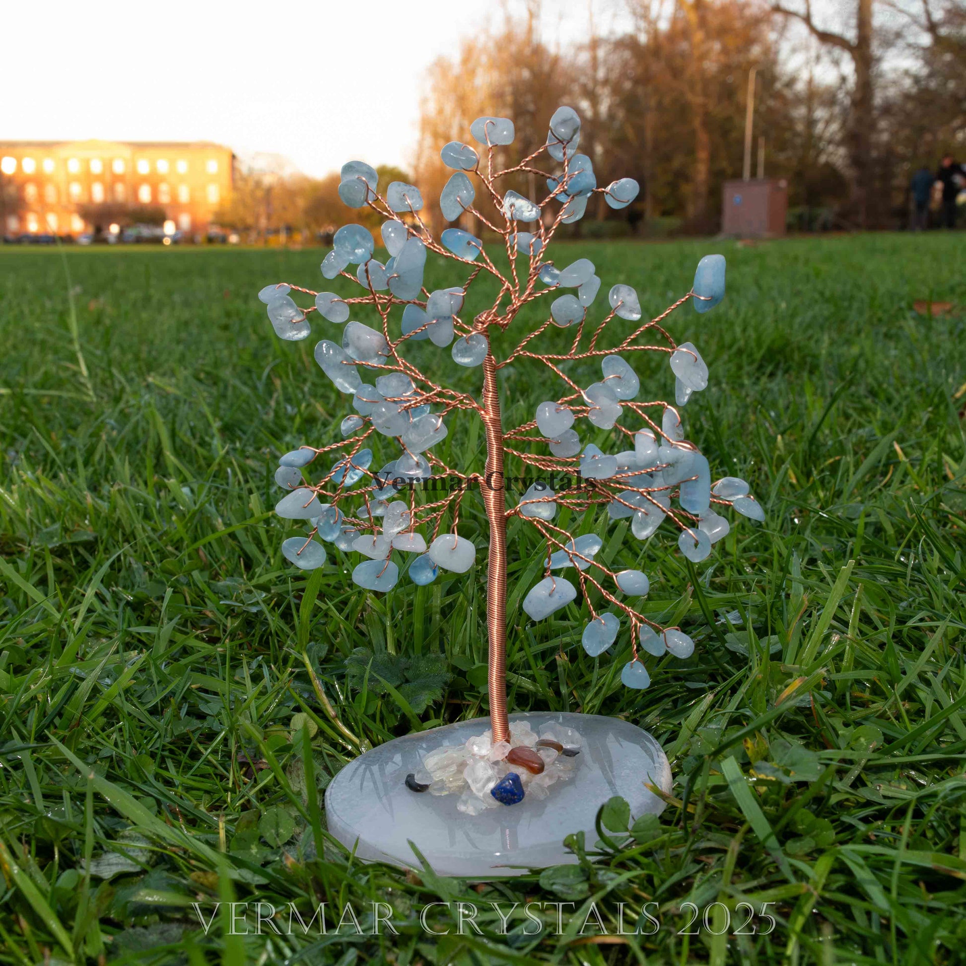 Handmade aquamarine crystal tree with natural blue gemstones and copper wire branches on round agate base outdoors on grass