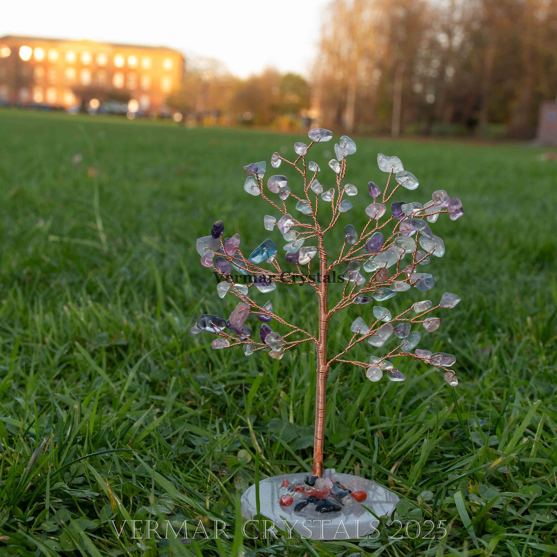 Handmade fluorite crystal tree ornament with multicolored stones and polished agate base on grass background