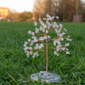 Handmade decorative tree with natural rose quartz crystal chips on copper wire and polished agate stone base on grass background