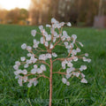 Handmade rose quartz crystal tree with delicate wire branches and small polished rose quartz gemstones on green grass background
