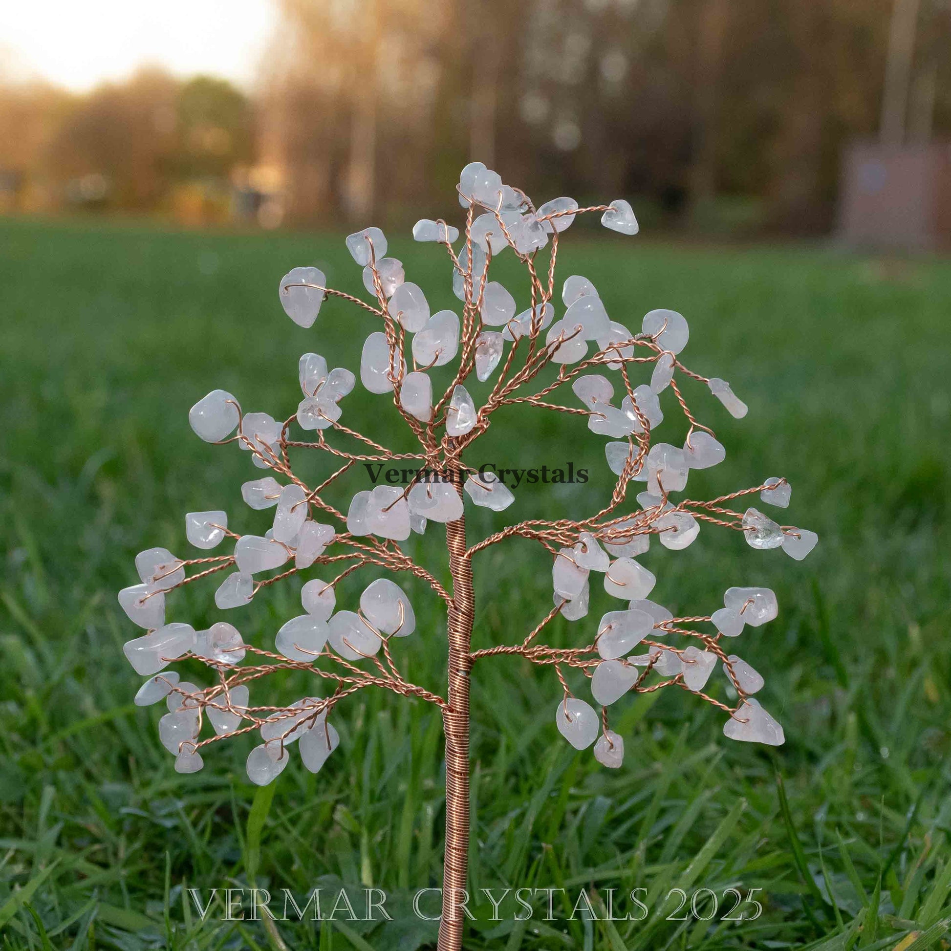 Handmade rose quartz crystal tree with delicate wire branches and small polished rose quartz gemstones on green grass background
