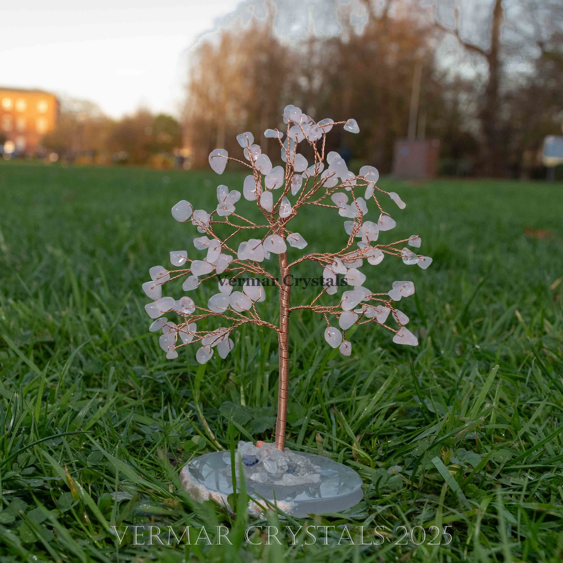 Handmade rose quartz crystal tree with polished chips on copper wire and natural agate base on grass outdoors