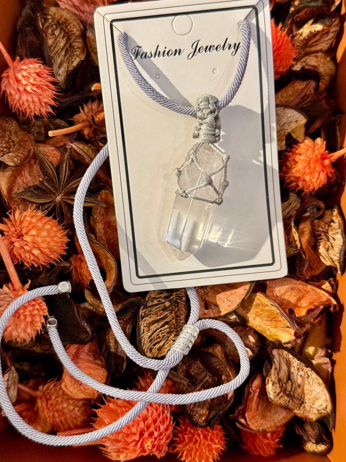 Raw clear quartz point pendant wrapped in white macramé cord on light gray background