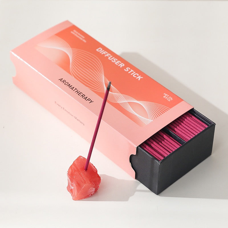 Box of pink aromatherapy diffuser sticks with one stick placed in a small natural stone incense holder on white surface