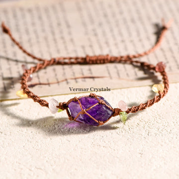 Handcrafted amethyst stone wrapped with brown macrame cord, accented with small pastel beads on textured surface and paper background