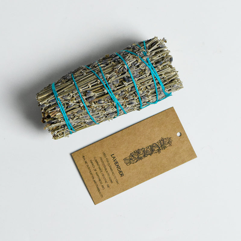 Hand-tied lavender smudge stick wrapped with turquoise string alongside a brown kraft paper tag on white background