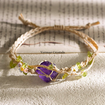 Handcrafted amethyst stone wrapped in braided cord with small flower and green bead accents on textured surface