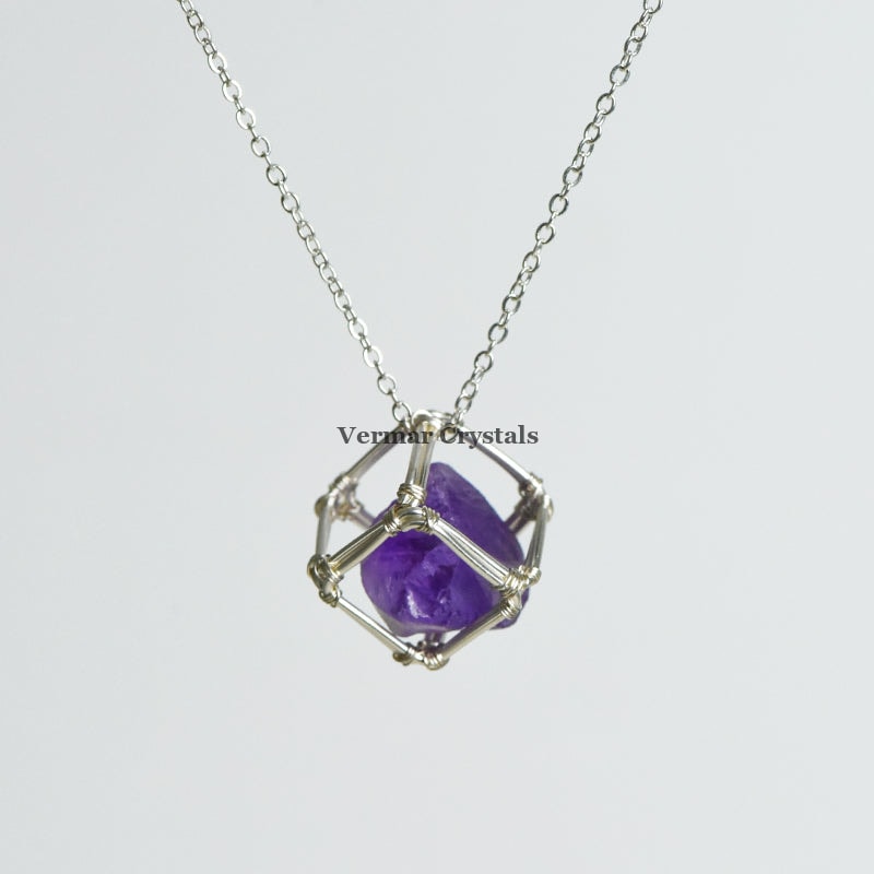 Handcrafted raw amethyst crystal pendant wrapped in silver wire cage on a delicate silver chain necklace against white background