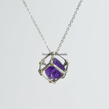 Handcrafted raw amethyst crystal pendant wrapped in silver wire cage on a delicate silver chain necklace against white background